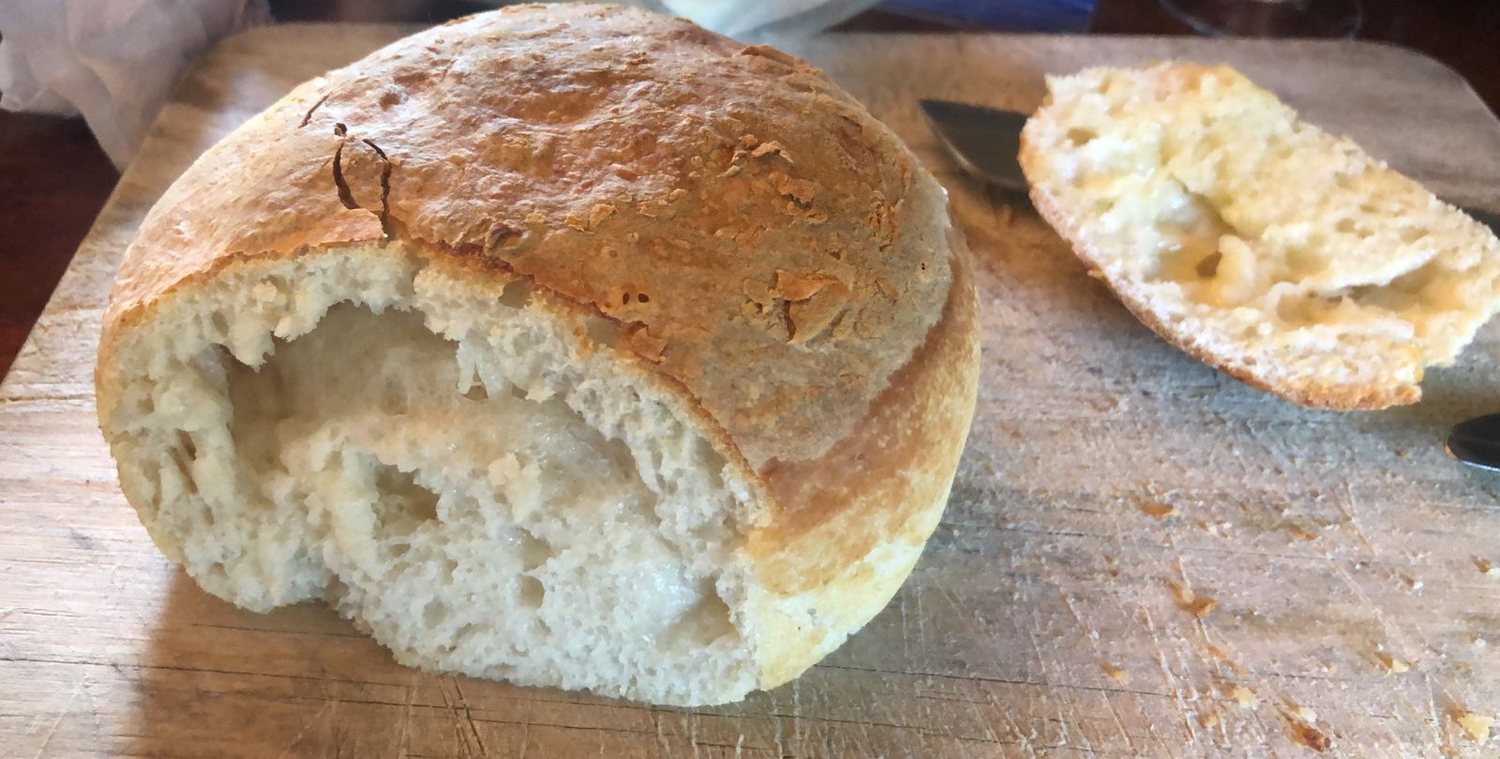 A torn-open loaf of homemade sourdough revealing a soft crumb, beside a slice spread with melting butter on a wooden board